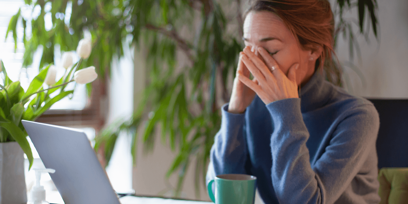 person working from home sitting in front of laptop rubbing their eyes