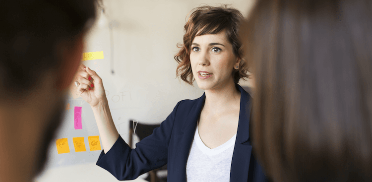 person pointing to sticky notes on a board and explaining something to coworkers