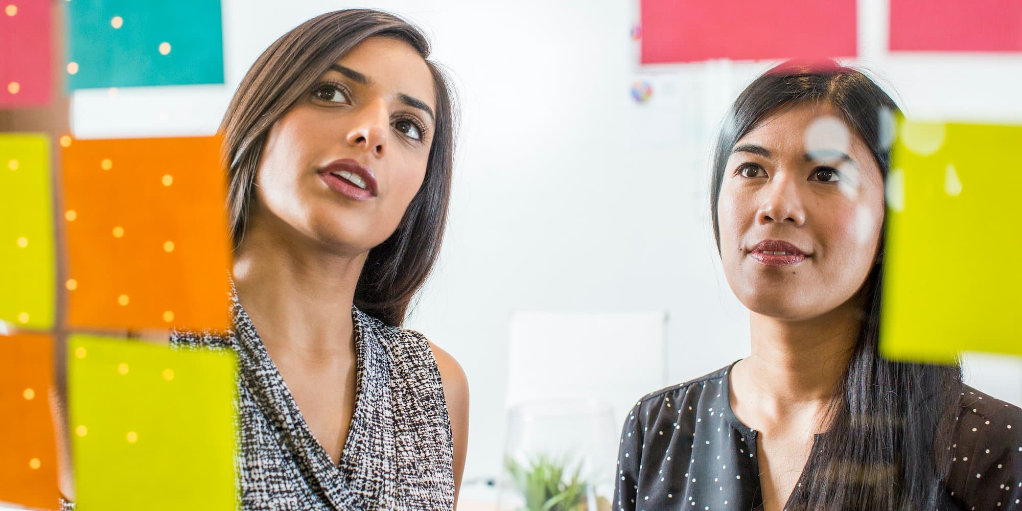 two people organize a project using sticky notes on a glass wall